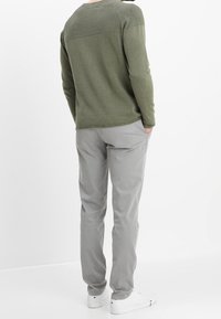 Olive green long-sleeve shirt with a textured finish paired with light gray pants, featuring a relaxed fit and white sneakers.