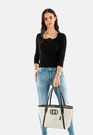 Borsa a spalla in canvas beige con dettagli e logo in pelle nera, abbinata a una maglietta nera aderente e jeans azzurri.