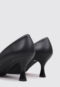 Zapatos de tacón alto de cuero negro con una forma elegante, que presentan un tacón curvado y una textura lisa. No se observan patrones ni detalles adicionales.