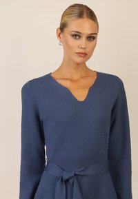 Abito lavorato a maglia blu con scollatura a V, maniche lunghe e cintura legata in vita. Tessuto liscio con corpino aderente e gonna a campana.