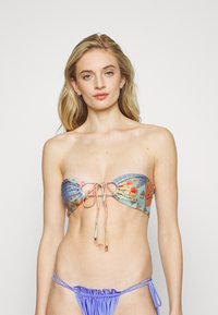 Top de bikini sem alças em tecido azul claro com padrão floral, apresentando um corte central e detalhes com laços; combinado com um fundo lavanda.