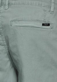 Pantalons bleu clair en tissu doux, avec une poche arrière dotée d'une étiquette portant la mention "STREET ONE" et des détails de couture soignés.