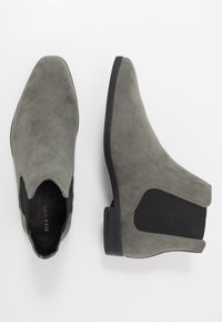 Botas de tornozelo em camurça cinza com painéis laterais elásticos e um salto baixo em borracha preta. Bico afunilado e detalhe de textura suave na parte superior.