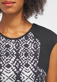 Vestido de patrón en blanco y negro con una tela texturizada. Presenta un yugo negro sólido y mangas cortas, exhibiendo intrincados diseños geométricos.
