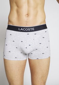 Sive boxerice izdelane iz mešanice bombaža, z malimi mornarskimi krokodilskimi logotipi, črn pas z napisom "LACOSTE" v beli barvi.