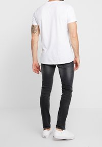 Vit kortärmad t-shirt med rund hals, matchad med svarta slim-fit jeans. Avslutat med vita sneakers med en mjuk yta.