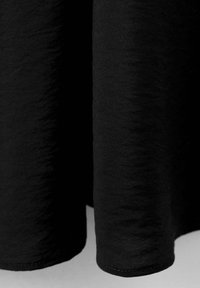 Gros plan sur l'ourlet d'un vêtement en tissu texturé noir, montrant les détails de la couture et le tissage du tissu.