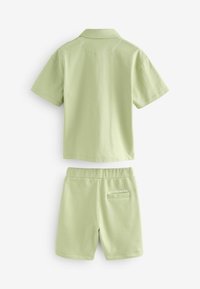 Lys grøn bomuld kortærmet poloshirt og matchende shorts. Poloshirten har krave, og shortsene har elastisk talje og baglomme.