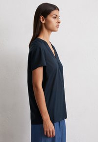 Navy blue, short-sleeve top with a V-neckline. Made of smooth fabric, features a relaxed fit with subtle draping at the front and sides.