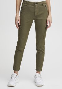 Pantalons cargo vert olive avec une coupe slim, dotés de poches zippées, d'une fermeture à bouton et d'ourlets à la cheville, associés à des baskets blanches.
