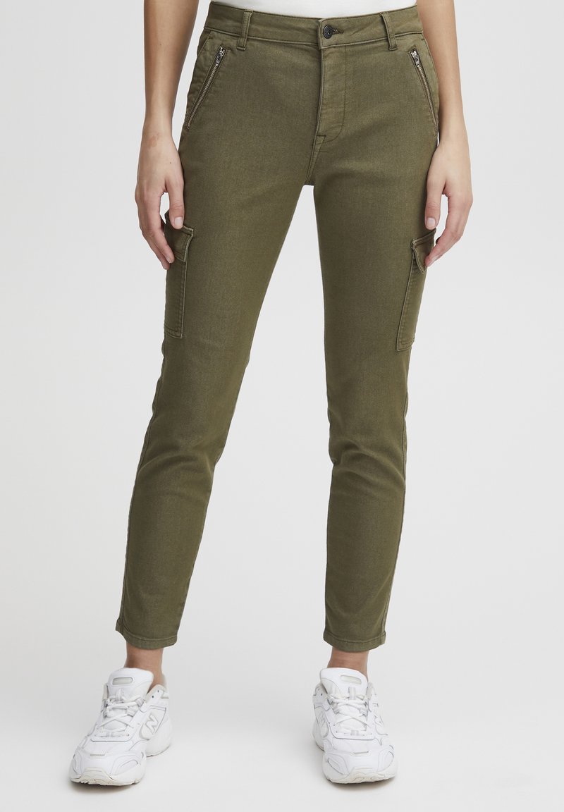 Pantalons cargo vert olive avec une coupe slim, dotés de poches zippées, d'une fermeture à bouton et d'ourlets à la cheville, associés à des baskets blanches.