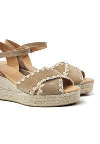 Beige suède wedge sandalen met kruislings strapjes, jute touwzolen en crèmekleurige stikselaccenten die het teengebied details geven.