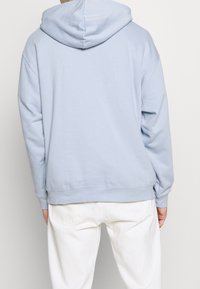 Sudadera azul claro hecha de una tela suave, con una capucha amplia y puños acanalados, combinada con pantalones blancos. Textura suave y diseño casual.