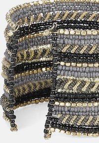 Brățară din mărgele care prezintă un amestec de mărgele negre, aurii și gri, cu modele intricate; design flexibil cu texturi stratificate.