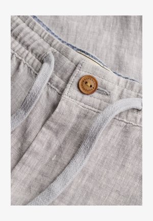 Pantalones de lino gris claro con un botón de madera etiquetado "Superdry" y cordones blancos en la cintura.