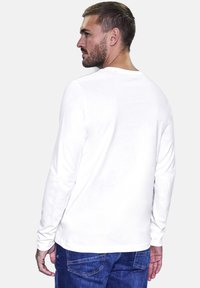 Vit bomullsskjorta med lång ärm, rund halsringning, avslappnad passform och subtila sömnadsdetaljer, i kombination med blå denimjeans.