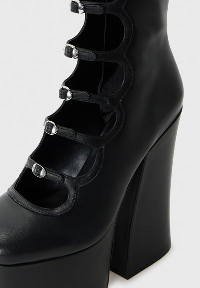 Chaussure à talons hauts noire avec plateforme, dotée de cinq brides argentées à boucle et d'un design découpé en forme de vagues sur le dessus.