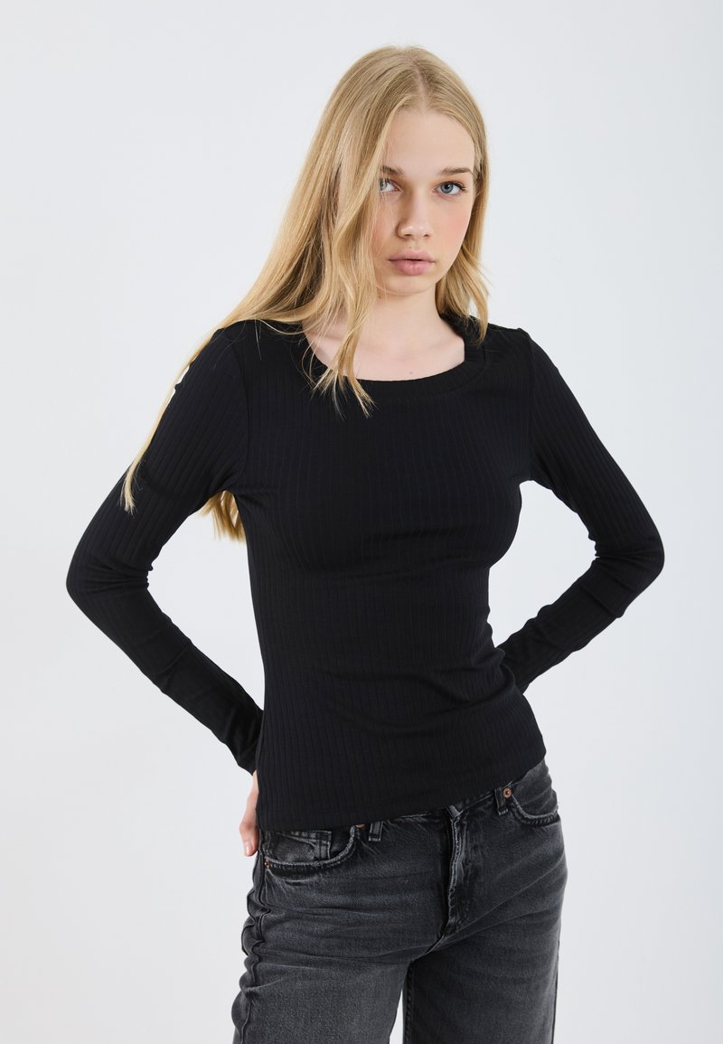 Zwarte lange mouwen geribbelde top met een ronde halslijn, nauwsluitend ontwerp en zachte textuur, gecombineerd met donkergrijze jeans.