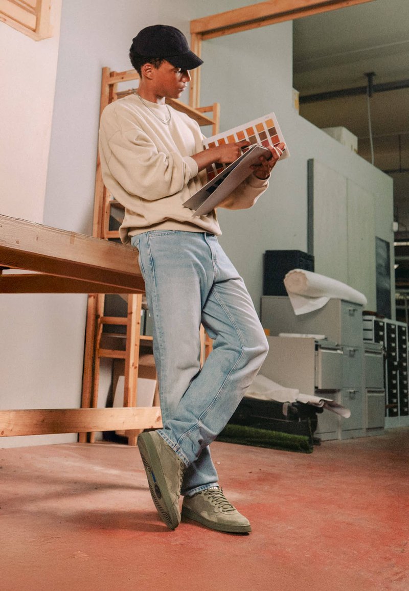 Jeune personne en vêtements décontractés se tient dans un atelier en comparant des échantillons de couleurs de peinture provenant d’un livret.
