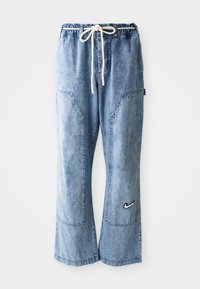 Pantalon en denim bleu clair avec jambes larges, taille élastique, cordon blanc, grandes poches latérales et logo Nike sur la jambe droite inférieure.