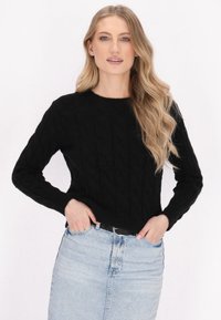 Maglione nero lavorato a maglia con motivo a trecce e maniche lunghe, abbinato a una gonna di jeans azzurro chiaro. Tessuto morbido, scollo rotondo.