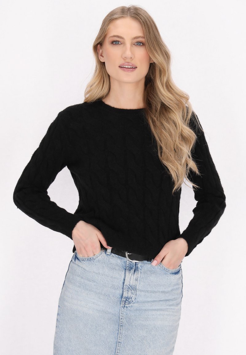 Maglione nero lavorato a maglia con motivo a trecce e maniche lunghe, abbinato a una gonna di jeans azzurro chiaro. Tessuto morbido, scollo rotondo.