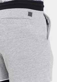 Grå bomuldsbukser har en sort talje, sidelomme og subtil tekstureret detaljering. Stoffet er blødt og let meleret.