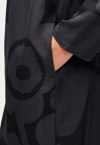 Μαύρο φόρεμα από ύφασμα με μεγάλο λουλουδένιο μοτίβο και διακριτή υφή. Διαθέτει πλαϊνή τσέπη στην αριστερή πλευρά.