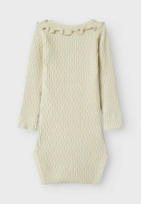 Langermet ribbestrikket heldrakt i lys kremfarge, med volangkant i halsen og sideknapper for enkel påkledning. Mykt, strukturert bomullsmateriale.