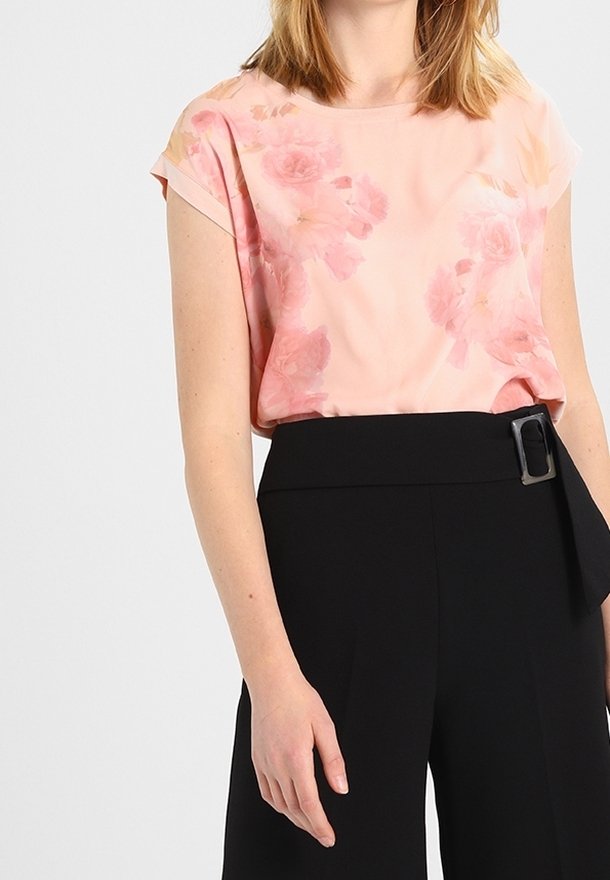 Haut rose clair avec imprimé floral, à manches courtes et col rond, associé à un pantalon noir taille haute avec un détail de boucle.