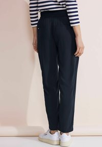 Marineblauwe lichtgewicht broek met een elastische tailleband, twee achterzakken en een rechte pijp. Draag met witte sneakers.