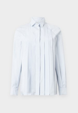 Camisa de manga longa azul clara com colarinho pontudo, apresentando pregas verticais na frente e fecho de botão no pescoço. Textura de tecido suave.