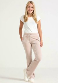 Light pink sweatpants with side pockets and a drawstring waist, paired with a white fitted t-shirt and white sneakers. Smooth texture.