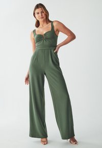 Groene jumpsuit met een aansluitende top, brede pijpen en een sleufdetail bij de borst. Gemaakt van een gladde, elastische stof.