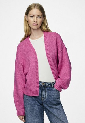 Cardigan lavorato a maglia rosa con vestibilità rilassata, polsini a costine, apertura frontale e tessuto testurizzato, abbinato a una maglietta bianca e jeans blu.