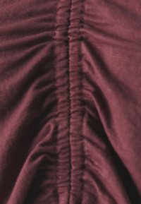 Tessuto bordeaux con texture arricciata in una cucitura centrale; superficie liscia con una leggera lucentezza e materiale morbido e leggero.
