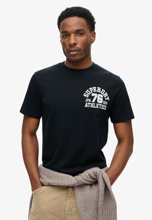 Schwarzes Baumwoll-T-Shirt mit kurzen Ärmeln, das auf der linken Brustseite ein weißes, gesticktes Logo "SUPERDRY 76 ATHLETICS" trägt.