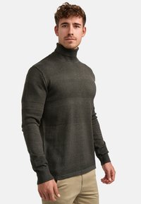 Mørkegrønn genser med høy hals og teksturerte paneler, lange ermer, ribbestrikkede mansjetter og kant. Laget av mykt strikket stoff.