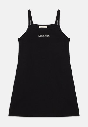 Svart ermeløs Calvin Klein-kjole med tynne stropper og hvit logo sentrert nær halslinningen på en ensfarget bakgrunn.
