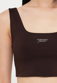 Brun ribbet crop topp med brede stropper og firkantet hals, med hvitt brodert "tommy jeans"-logo på fronten.
