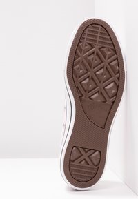 Podeszwa białego trampka Converse All Star z brązową teksturowaną podeszwą o geometrycznych wzorach oraz wyraźnie widocznym logo marki.
