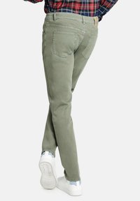 Pantalones de algodón verde claro con un ajuste slim, que cuentan con bolsillos traseros y una etiqueta de piel en la cintura. Combinados con zapatillas blancas.