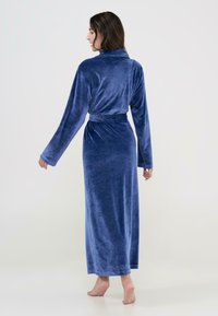 Ropa larga de terciopelo azul con un collar relajado, mangas largas y una cintura atada. Textura suave y diseño hasta el suelo.