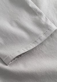 Tela tejida de color gris claro con una superficie texturizada, que presenta un acabado suave y un dobladillo cosido con cuidado.