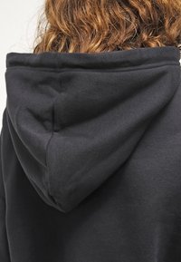 Zwarte hoodie met een afgeronde, gladde capuchon. De stof lijkt zacht en gevarieerd, met subtiele stiksels.