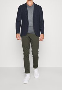 Námořnický blazer s klopami, šedé tričko s véčkovým výstřihem, olivově zelené chinos kalhoty a bílé tenisky; uvolněný střih, hladká textura, minimální detaily.