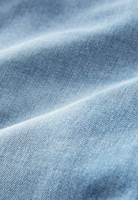 Tela de mezclilla de color azul claro con una textura suave y ligero elasticidad. La superficie muestra variaciones sutiles y un patrón de tejido áspero.