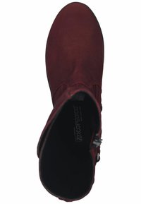 Botín de ante rojo con punta redonda, cremallera lateral y textura suave. Suela negra con la marca visible en la plantilla.