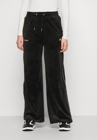 Svarta sammet breda byxor med gyllene detaljer och dragsko i midjan. Har varumärkets logo på fickan och sidostrimma. Slät textur.