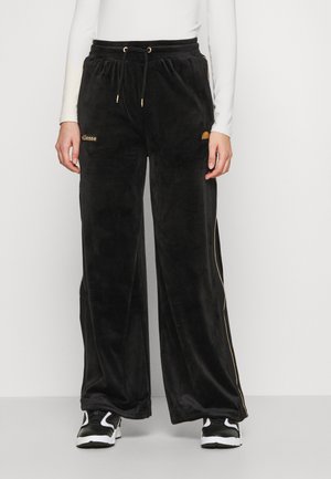 Musta samettiset leveälahkeiset housut, joissa on kultaiset yksityiskohdat ja nauhakuja. Tyylissä on brändin logo taskussa ja sivujen kaarrokkeet. Sileä pinta.